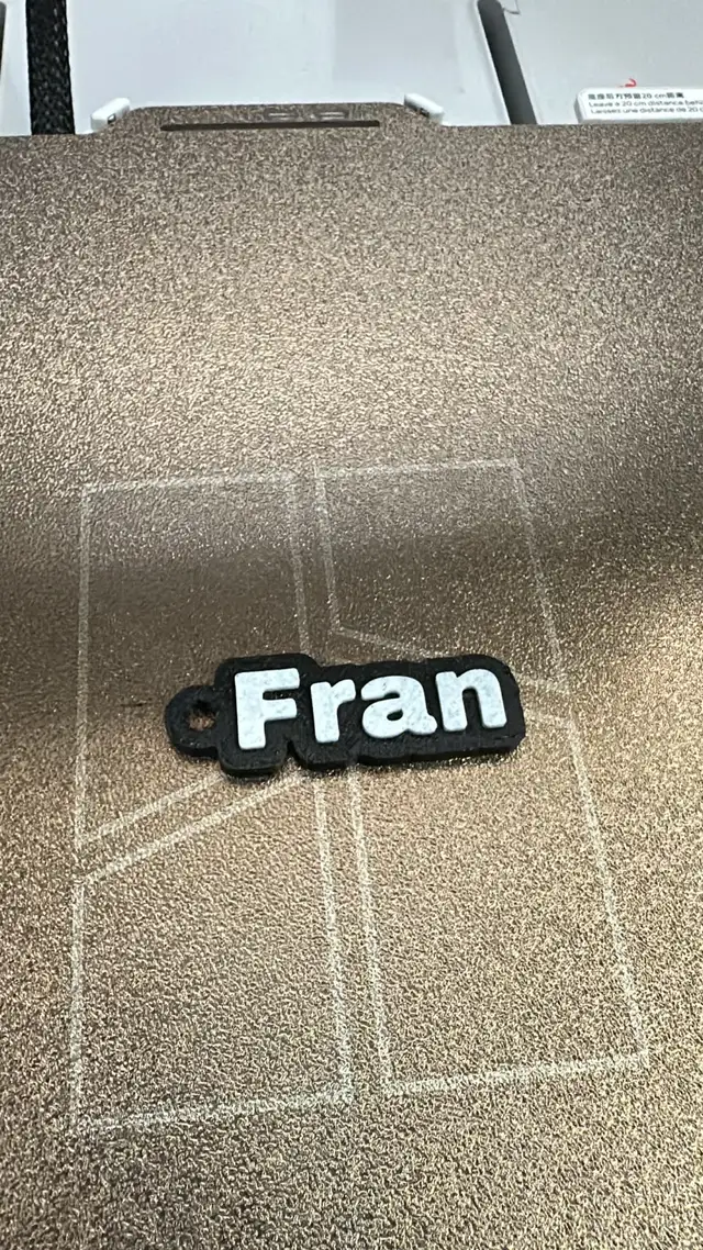 Llavero con el nombre Fran visto desde arriba sobre la cama texturada de la impresora 3D